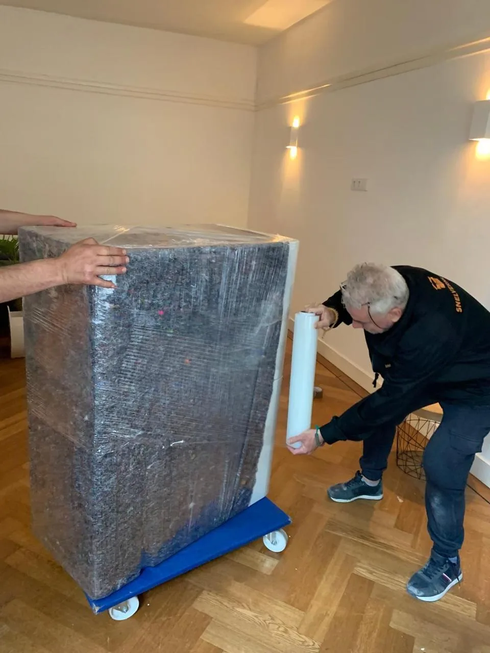 Verhuizer wikkelt een kast in verhuisdeken en folie